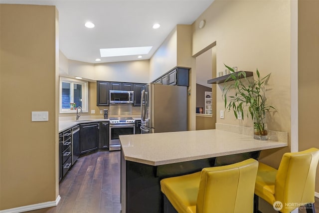 kitchen with stainless steel appliances, a sink, a skylight, a peninsula, and dark wood-style floors