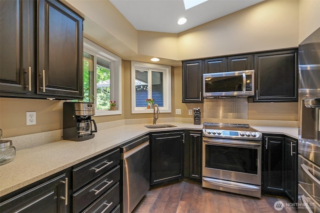 kitchen with appliances with stainless steel finishes, a sink, a skylight, dark wood-type flooring, and light stone countertops