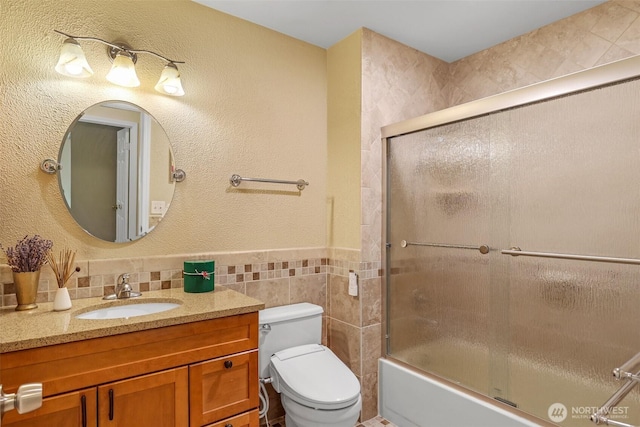 full bathroom with vanity, toilet, tile walls, shower / bath combination with glass door, and wainscoting