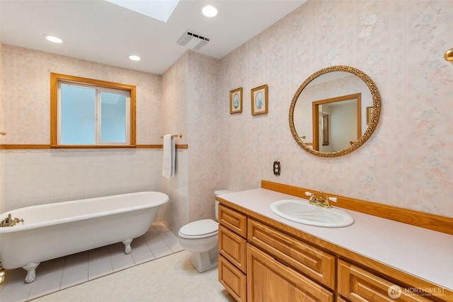 full bath featuring a freestanding bath, tile patterned floors, toilet, vanity, and wallpapered walls
