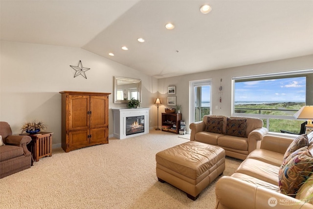 living area with recessed lighting, a glass covered fireplace, vaulted ceiling, and light carpet