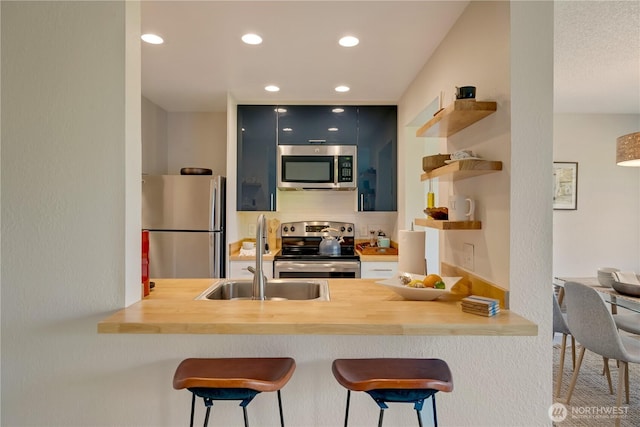 kitchen featuring appliances with stainless steel finishes, a sink, a peninsula, open shelves, and a breakfast bar area