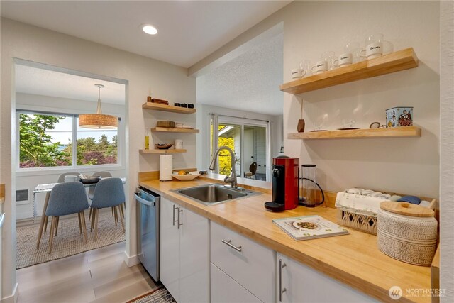 kitchen featuring open shelves, stainless steel dishwasher, a sink, white cabinets, and wood counters