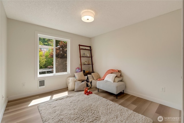 living area featuring light wood finished floors, baseboards, and a textured ceiling