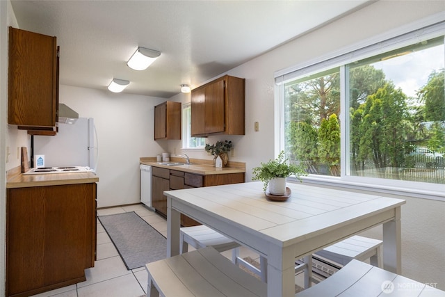 kitchen featuring light tile patterned floors, light countertops, dishwasher, brown cabinets, and a sink