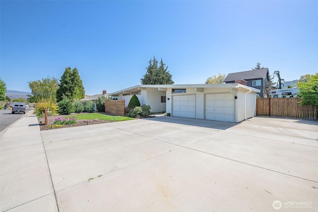 view of front facade featuring an attached garage, concrete driveway, and fence