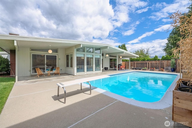 view of swimming pool featuring a patio, a diving board, and fence