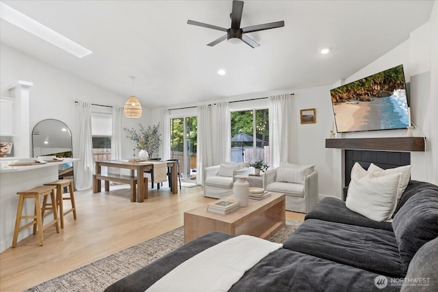 living room with vaulted ceiling, light wood-type flooring, ceiling fan, a skylight, and recessed lighting