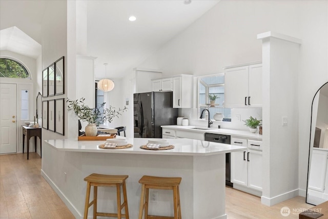 kitchen with dishwasher, black fridge, a sink, light wood-style floors, and white cabinetry