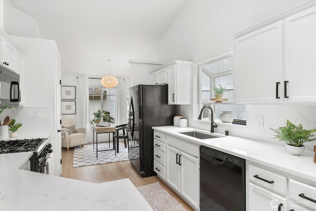 kitchen with black appliances, a sink, backsplash, white cabinetry, and light wood-type flooring
