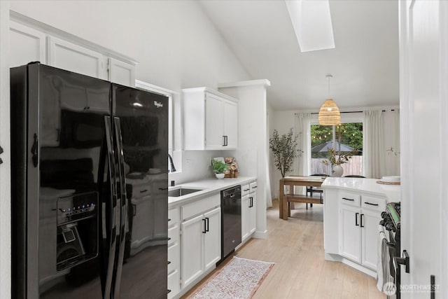kitchen with black appliances, white cabinets, a skylight, light countertops, and lofted ceiling