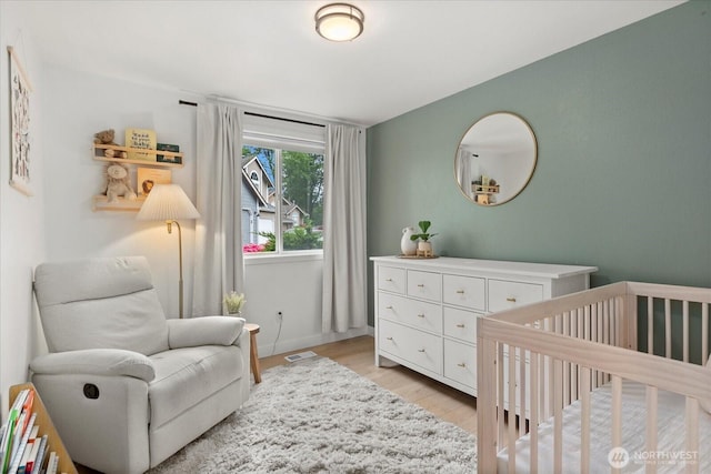 bedroom with a crib, light wood-style floors, and baseboards