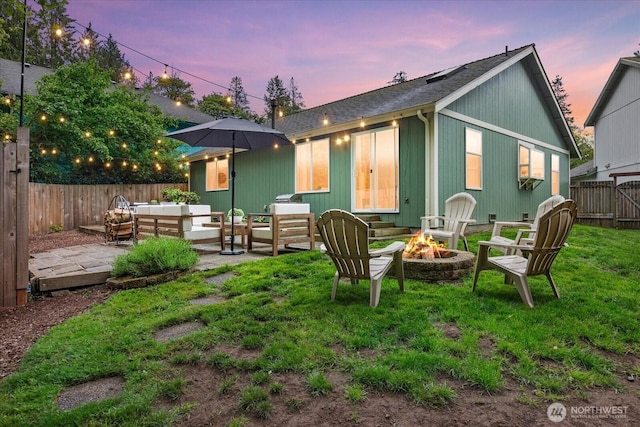 back of property at dusk featuring an outdoor living space with a fire pit, a patio area, and a shingled roof
