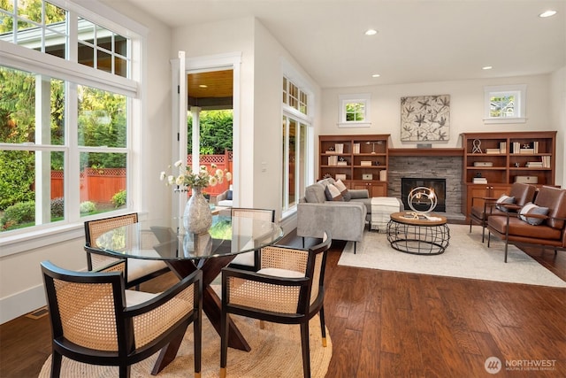 dining space with recessed lighting, wood finished floors, a stone fireplace, and baseboards