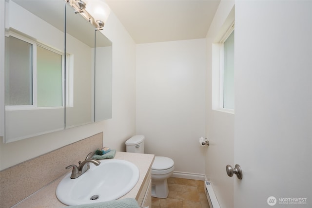 half bath with toilet, a baseboard heating unit, vanity, and plenty of natural light
