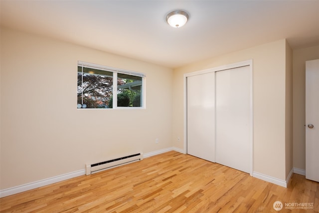 unfurnished bedroom with a baseboard heating unit, wood finished floors, a closet, and baseboards