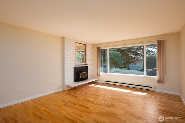 unfurnished living room with a baseboard heating unit, a wood stove, wood finished floors, and baseboards