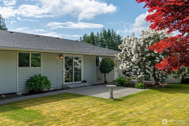 rear view of property with a patio, roof with shingles, and a yard