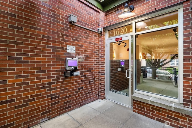 entrance to property featuring brick siding and a security system