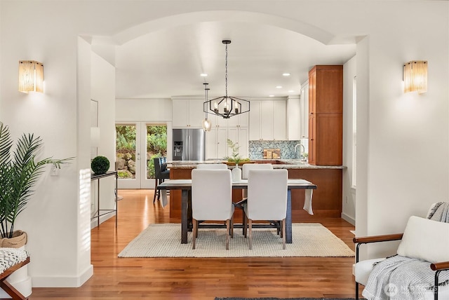 dining room with light wood-type flooring, a chandelier, baseboards, recessed lighting, and arched walkways