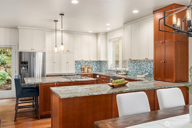 kitchen featuring stainless steel appliances, a peninsula, brown cabinets, light stone counters, and backsplash