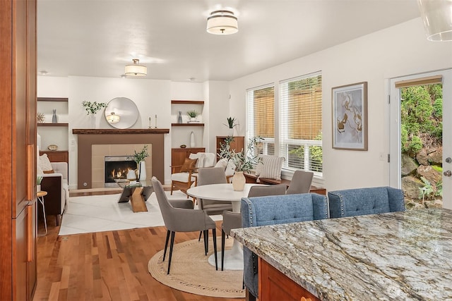 dining area featuring light wood-type flooring, a tiled fireplace, and built in shelves
