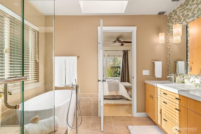 ensuite bathroom featuring a skylight, tile patterned floors, vanity, a freestanding bath, and ceiling fan