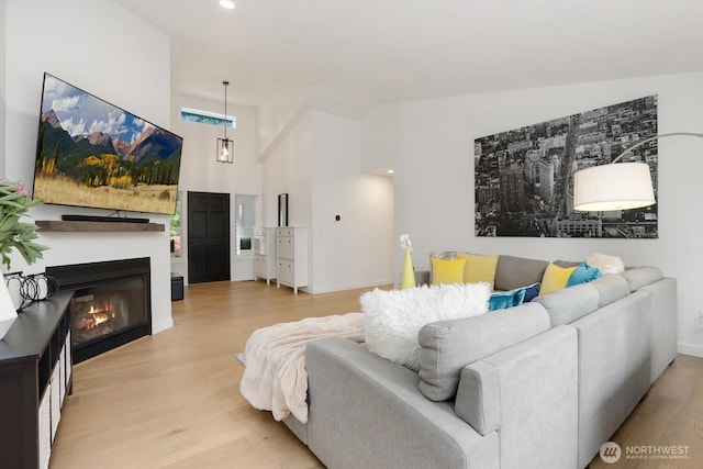 living area featuring light wood finished floors, a glass covered fireplace, baseboards, recessed lighting, and high vaulted ceiling