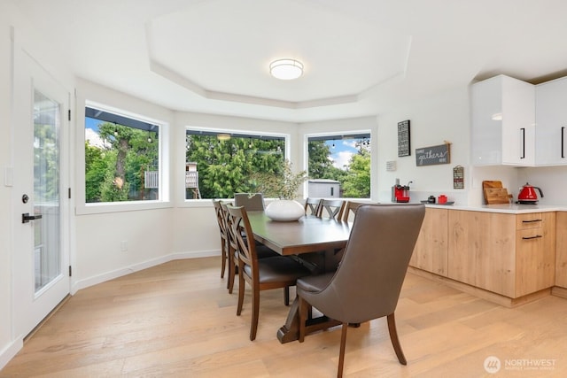 dining area with light wood-type flooring, a tray ceiling, and baseboards