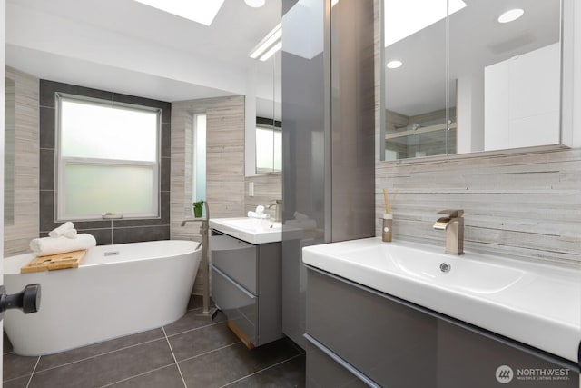 bathroom with tile walls, two vanities, tile patterned floors, and a freestanding bath