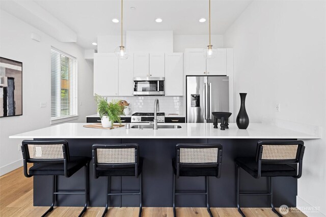 kitchen with stainless steel appliances, a sink, white cabinets, backsplash, and decorative light fixtures