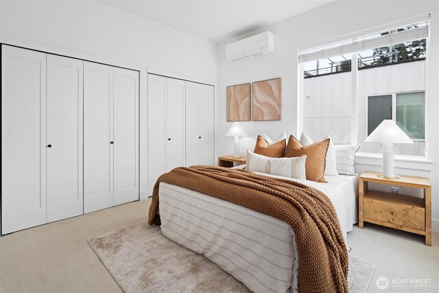 bedroom featuring two closets, a wall mounted air conditioner, and light colored carpet