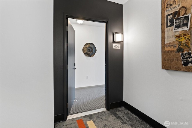 hallway featuring baseboards and dark carpet