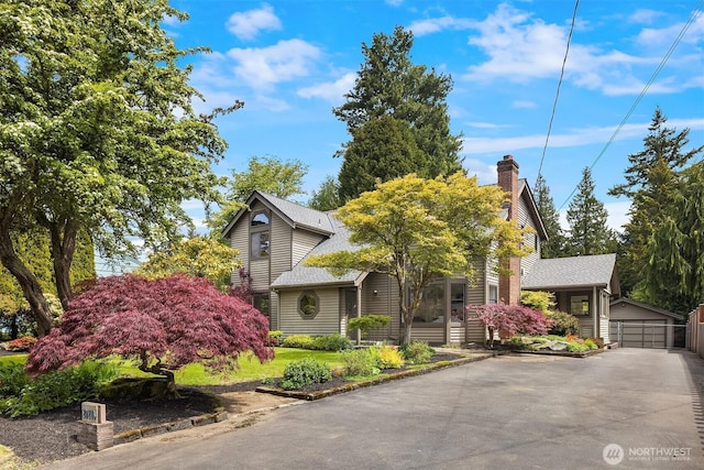 view of property hidden behind natural elements with a shingled roof, a detached garage, and a chimney