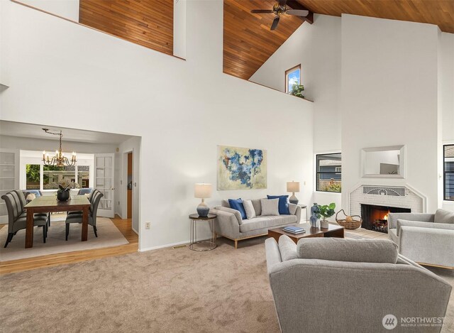 carpeted living room featuring high vaulted ceiling, a chandelier, a fireplace, baseboards, and ceiling fan