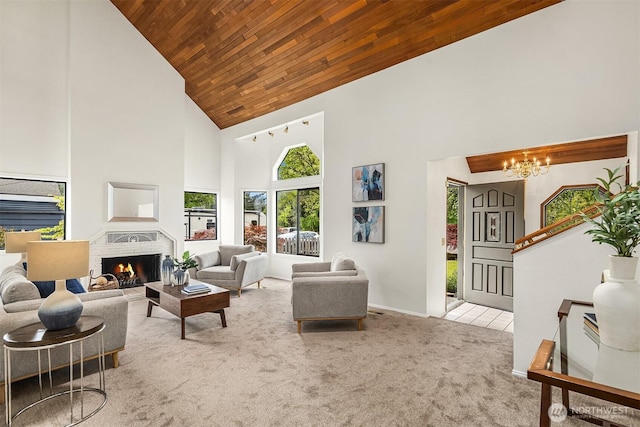 carpeted living area with high vaulted ceiling, wooden ceiling, a chandelier, a fireplace, and baseboards
