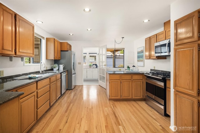 kitchen featuring stainless steel appliances, a sink, light wood-type flooring, a peninsula, and brown cabinetry