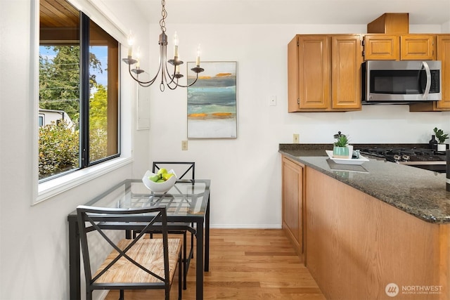 kitchen with stainless steel microwave, a chandelier, light wood finished floors, dark stone counters, and baseboards