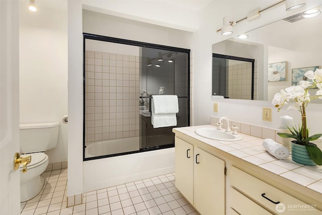 bathroom with toilet, vanity, tile patterned floors, and bath / shower combo with glass door
