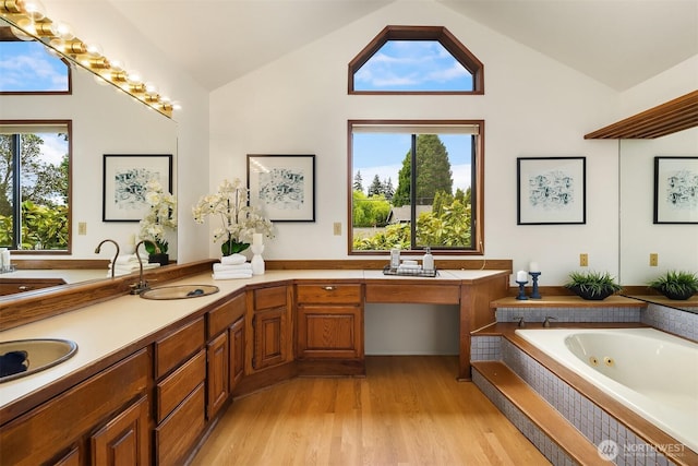 bathroom with a jetted tub, wood finished floors, high vaulted ceiling, and double vanity