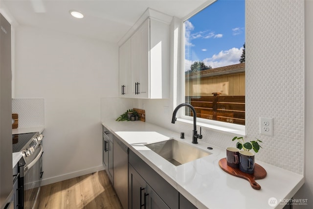 kitchen with a sink, stainless steel electric range oven, decorative backsplash, light wood-style floors, and light countertops