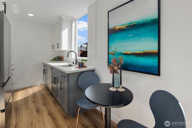 kitchen featuring a sink, light wood-style flooring, gray cabinetry, light countertops, and baseboards