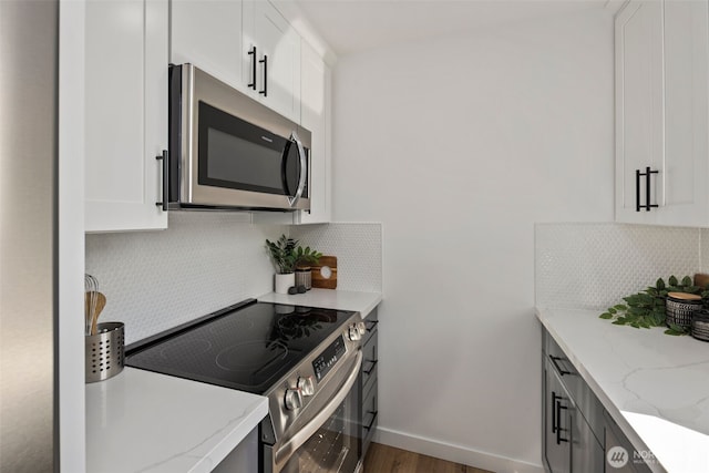 kitchen featuring appliances with stainless steel finishes, decorative backsplash, white cabinetry, light stone counters, and wood finished floors