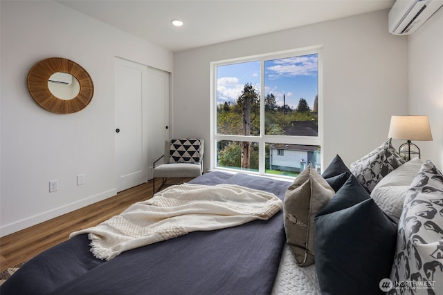 bedroom featuring a wall mounted AC, wood finished floors, baseboards, a closet, and recessed lighting