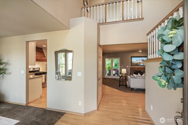 foyer entrance with light wood-type flooring, a towering ceiling, a fireplace, and baseboards