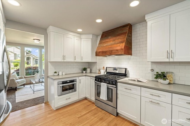 kitchen featuring appliances with stainless steel finishes, premium range hood, recessed lighting, white cabinets, and light wood-type flooring