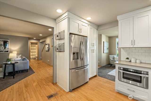 kitchen with appliances with stainless steel finishes, light wood finished floors, open floor plan, white cabinets, and recessed lighting