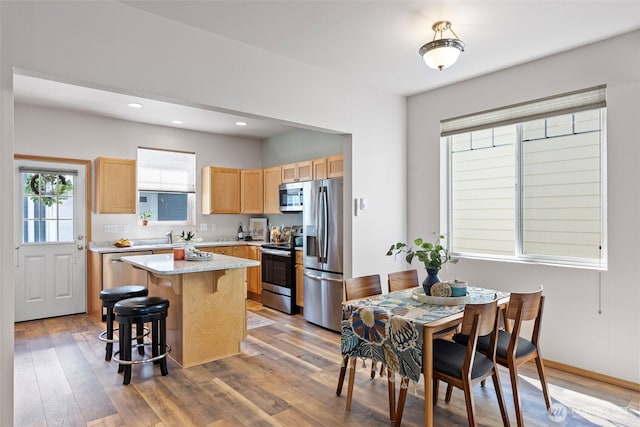 19554 Jensen Way NE, Poulsbo, WA 98370 - kitchen with stainless steel appliances, light brown cabinetry, a kitchen island, a breakfast bar, and light wood finished floors