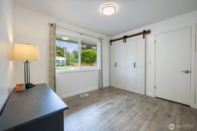 19045 Nutmeg St SW, Rochester, WA 98579 - unfurnished bedroom with light wood-style floors, baseboards, a textured ceiling, and a barn door