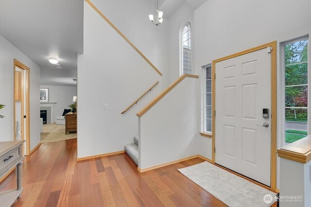entrance foyer featuring light wood-style floors, stairway, a chandelier, a fireplace, and a towering ceiling
